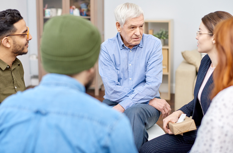 A clinical staff member providing guidance to adults during a Fairweather Lodge Program psychosocial rehabilitation session.